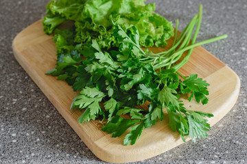 Fresh herbs, lettuce and parsley on a wooden cutting board on a gray granite background