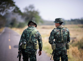 Asian army soldier return to base after completing military mission. Armed infantry walking in the foreground. Soldiers walking away on road concept.