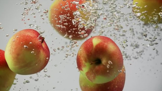 Apples red and yellow falling in water spinning and rotating with air bubbles white background