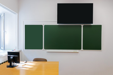 Blank chalkboard, blackboard hanging on the white wall with copy space. Computer on the teacher table and TV on the wall above board
