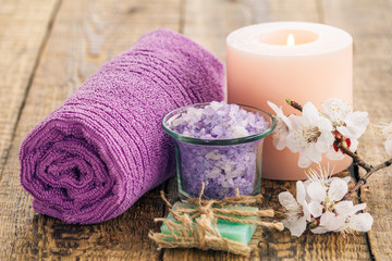 Obraz na płótnie Canvas Soap, sea salt in glass bowl with rolled towel and burning candle with flowering branch of apricot tree