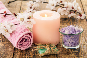 Fototapeta na wymiar Handmade soap, sea salt in glass bowl with rolled towel and burning candle with flowering branch of apricot tree