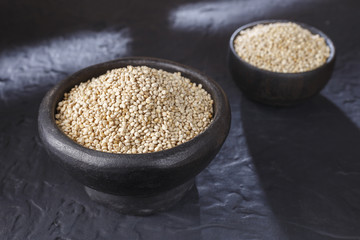 Quinoa grains with spoon and bowl on black background