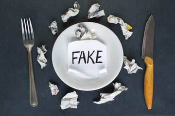 Word Fake written on a sheet of paper and scraps of newspapers on the dark background.