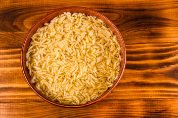 Ceramic bowl with prepared instant noodles on wooden table. Top view