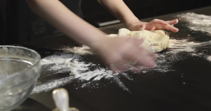 Close up view of children's hands kneading the dough on the table.