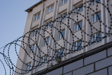 The barbed wire is taut on the fence with coils on the background of the building