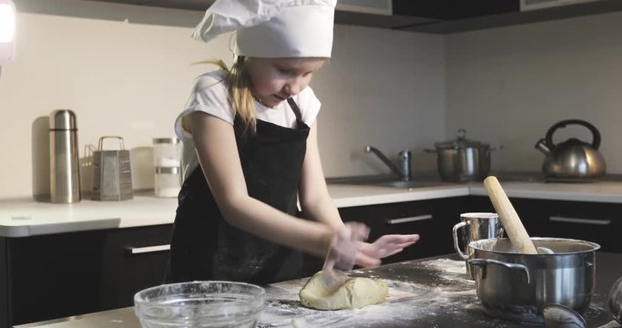 Beautiful girl chef rolls the dough on the table with the help of a rolling pin.