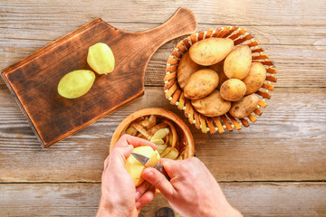 Men's hands clean potatoes for okroshki on an old wooden table.