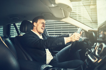 Smilng businessman singing while driving his car through the cit