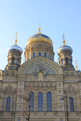 Fototapeta na wymiar Church of the Assumption of Blessed Virgin Mary in St. Petersburg, Russia. Religious Russian Orthodox Cathedral Building, Exterior View with Facade and Domes from the Street with tree and Lantern.