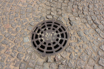 Manhole on Old Historical Cobblestone Street. Stone Textured Pavement and Manhole with Metal Cover on City Street. 