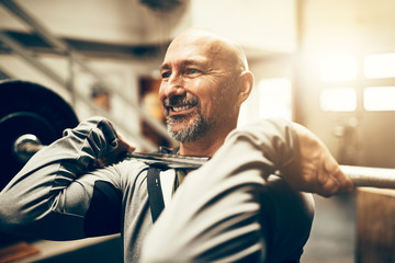 Fit mature man smiling and lifting weights in a gym