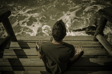 Hombre sentado sobre el muelle de madera meditando  con el yoga