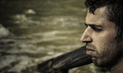 Retrato de hombre joven sentado en el muelle de madera al lado del mar