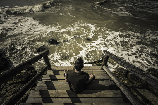 Hombre sentado sobre el muelle de madera meditando  con el yoga