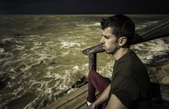 Hombre joven sentado en el muelle frente al mar con temporal