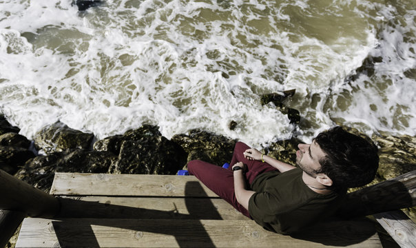 Hombre joven sentado en el muelle mirando al mar