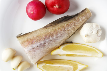 Fish, slice lemon, cloves of garlic and radish on white background. Uncooked natural ingredients closeup. Top view
