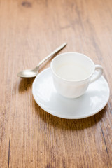 white coffee cup with coffee stains next to spoon and on wooden background