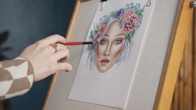 Close-up makeup of women's hands, which draws a sketch of the facial diagram. The girl artist paints a sketch on the face of the charts. Young woman in a bright studio draws a face chart using