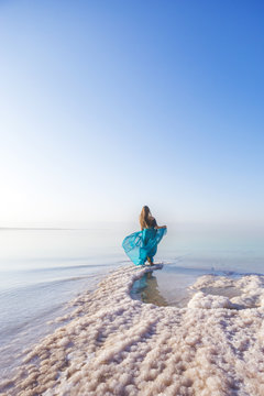 Blonde young woman in a blue dress on the shore of the dead sea. Jordan