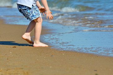 A boy in yellow glasses touches the wet sand near the blue sea