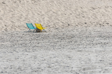 A blue and yellow folding chair on a beach.