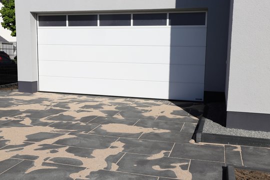 Modern gepflasterter Hofeinfahrt mit wei&szlig;em Garagentor