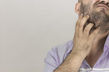 Fototapeta premium A man scratching his beard. Closeup to mature man scratching beard, thoughtful gesture, indoors studio shot