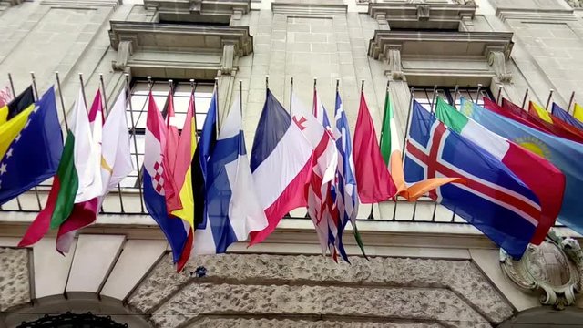 International flags from OSCE and several nations waving in the wind in front of a historical building
