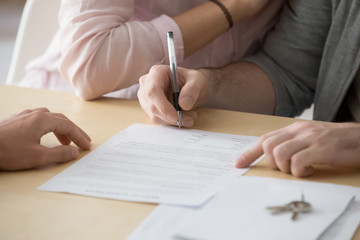 Couple renters tenants signing rental agreement renting new house, customers buyers put signature...