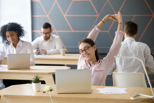 Millennial employee taking break from computer, young businesswoman or student stretching at workplace in multiracial coworking, relaxed manager happy to finish work enjoying pause for relaxation