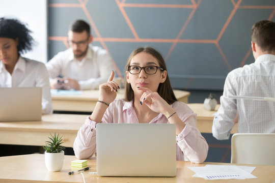 Thoughtful young woman puts finger up thinking of interesting creative idea sitting with laptop in coworking office, intelligent millennial employee or student found new business solution concept