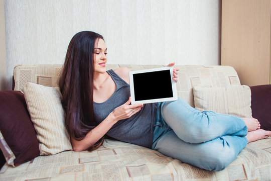A girl shows a tablet screen sitting on a beige sofa
