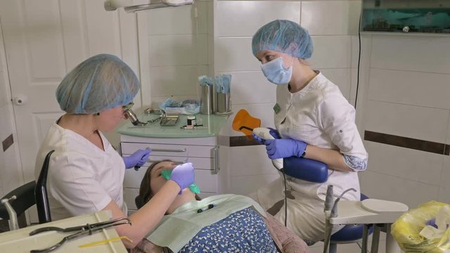 Woman at dentist clinic gets dental treatment to fill a cavity in a tooth. Dental restoration and composite material polymerization with UV light and laser. The doctor works with an assistant.
