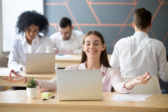 Calm smiling woman practicing office meditation in coworking space taking break for relaxation, mindful happy millennial student or employee feeling zen enjoying no stress free relief at work concept