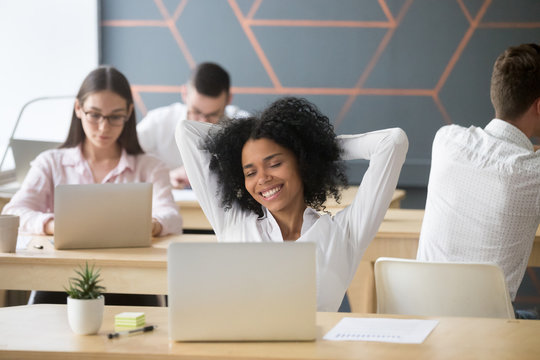 Smiling relaxed african american woman resting after computer work in office hands behind head, happy black employee student enjoying break stretching feeling no stress free relaxing in coworking