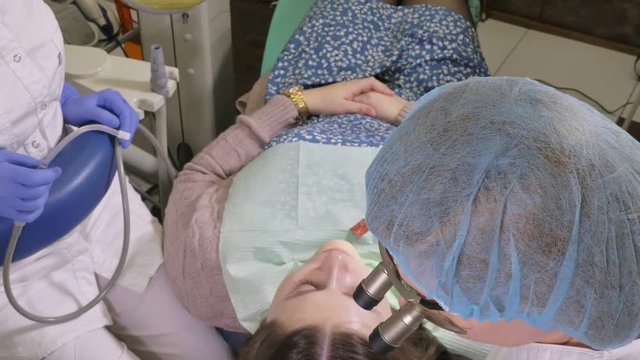 Woman at dentist clinic gets dental treatment to fill a cavity in a tooth. Dental restoration and composite material polymerization with UV light and laser. The doctor works with an assistant.