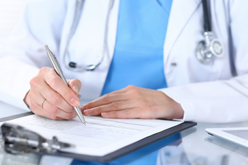 Female doctor filling up medical form by silver pen, closeup.  Physician sitting at the glass table in hospital office. Healthcare, insurance and medicine concept