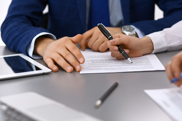 Group of business people and lawyer discussing contract papers sitting at the table, closeup. Businessman is signing document after agreement done