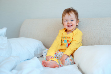 Funny little baby girl sitting in parents bed. Infant girl in yellow pajamas