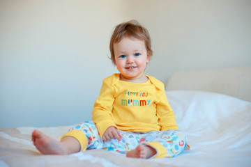 Funny little baby girl sitting in parents bed. Infant girl in yellow pajamas