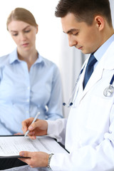 Fototapeta premium Male doctor holding application form while consulting female patient in hospital office. Perfect service in medicine and healthcare concept