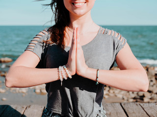 Young beautiful sporty woman doing yoga mudra on sea wooden beach near water. Girl practicing...