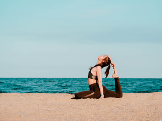 Young beautiful sporty woman in green clothing doing yoga asana on sea sandy beach near water. Girl practicing exercises. Health concept. Copy space.