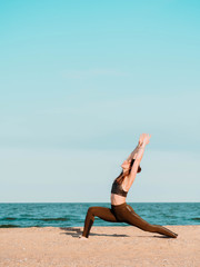 Fototapeta na wymiar Young beautiful sporty woman in green clothing doing yoga asana on sea sandy beach near water. Girl practicing exercises. Health concept. Copy space.