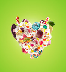 Heart form from whipped cream with sweets, jellies, heart front view. Crazy freakshake food trend. Front view of whipped heart of cream, full of berry and jelly sweets, chocolate candy. Colored