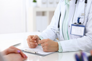 Doctor and patient talking while sitting at the desk in hospital office, closeup of human hands. Medicine and health care concept