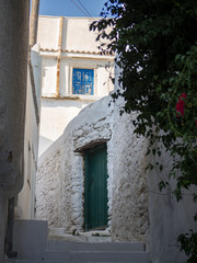 Fototapeta na wymiar A narrow alley in Amorgos with its white stairs, a green door and a blue window